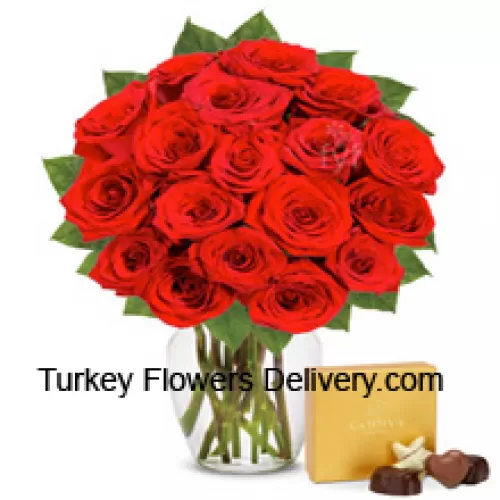 24 czerwone róże z kilkoma paprotkami w szklanym wazonie, w towarzystwie importowanego pudełka czekoladek