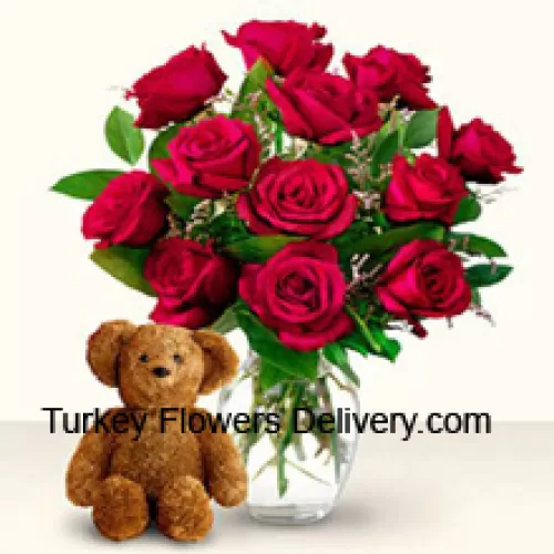 12 punaista ruusua joissa hieman saniaisia lasimaljakossa yhdessä suloisen 12 tuuman korkuisen ruskean teddyn kanssa