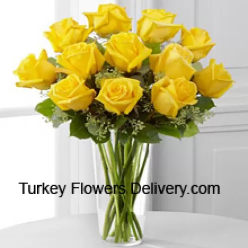 12 keltaista ruusua muutamien saniaisten kera lasimaljakossa