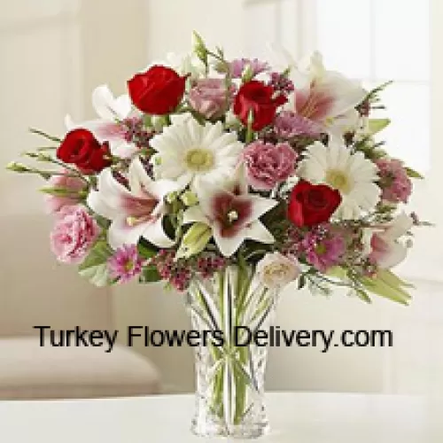 Punaiset ruusut, vaaleanpunaiset neilikat, valkoiset gerberat ja valkoiset liljat muiden erilaisten kukkien kanssa lasimaljakossa